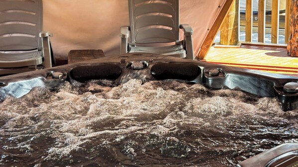A hot tub with water jets, surrounded by chairs and a wooden deck.