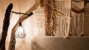 Ein Bett mit einer gestreiften Decke, einem Kopfteil mit Makramee-Verzierung und einer hängenden Leuchte.