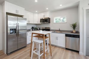 A modern kitchen with white cabinets, stainless steel appliances, a wooden table, and a bar stool.