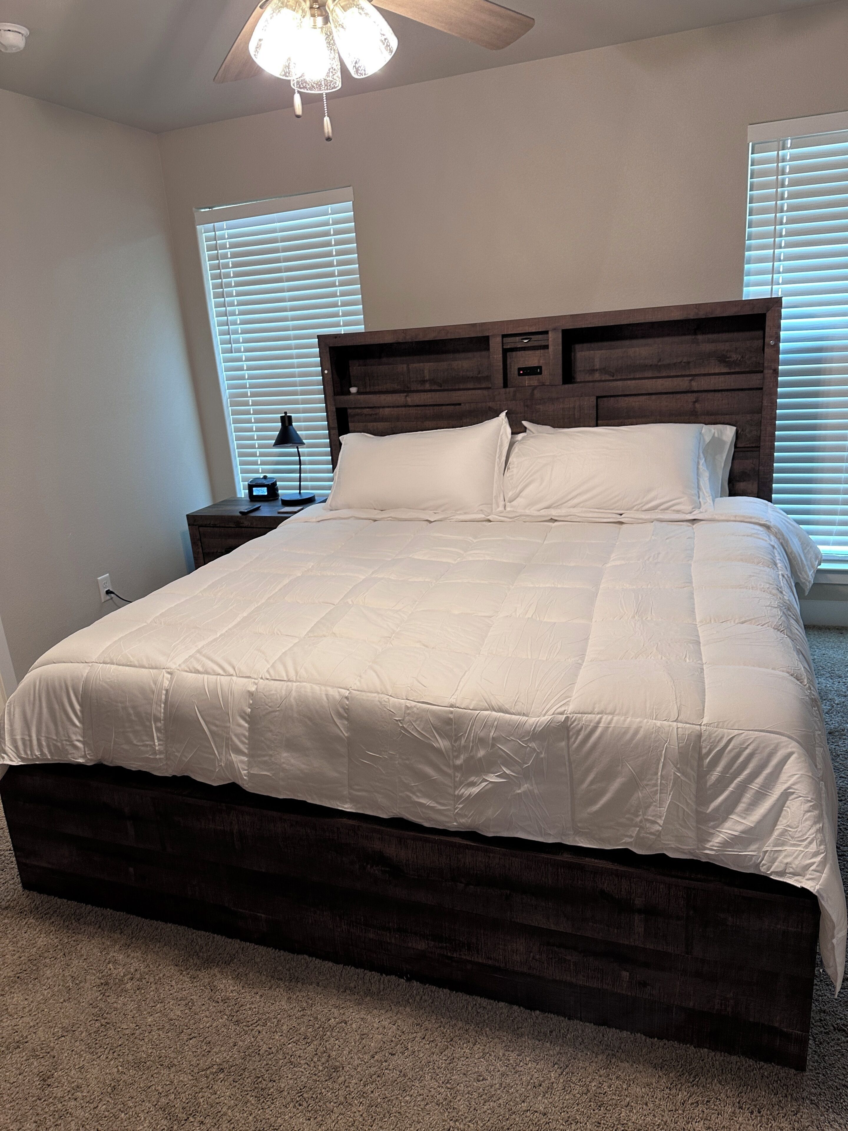 Une chambre à coucher avec un grand lit, une tête de lit en bois, une table de chevet, une lampe et un ventilateur de plafond.