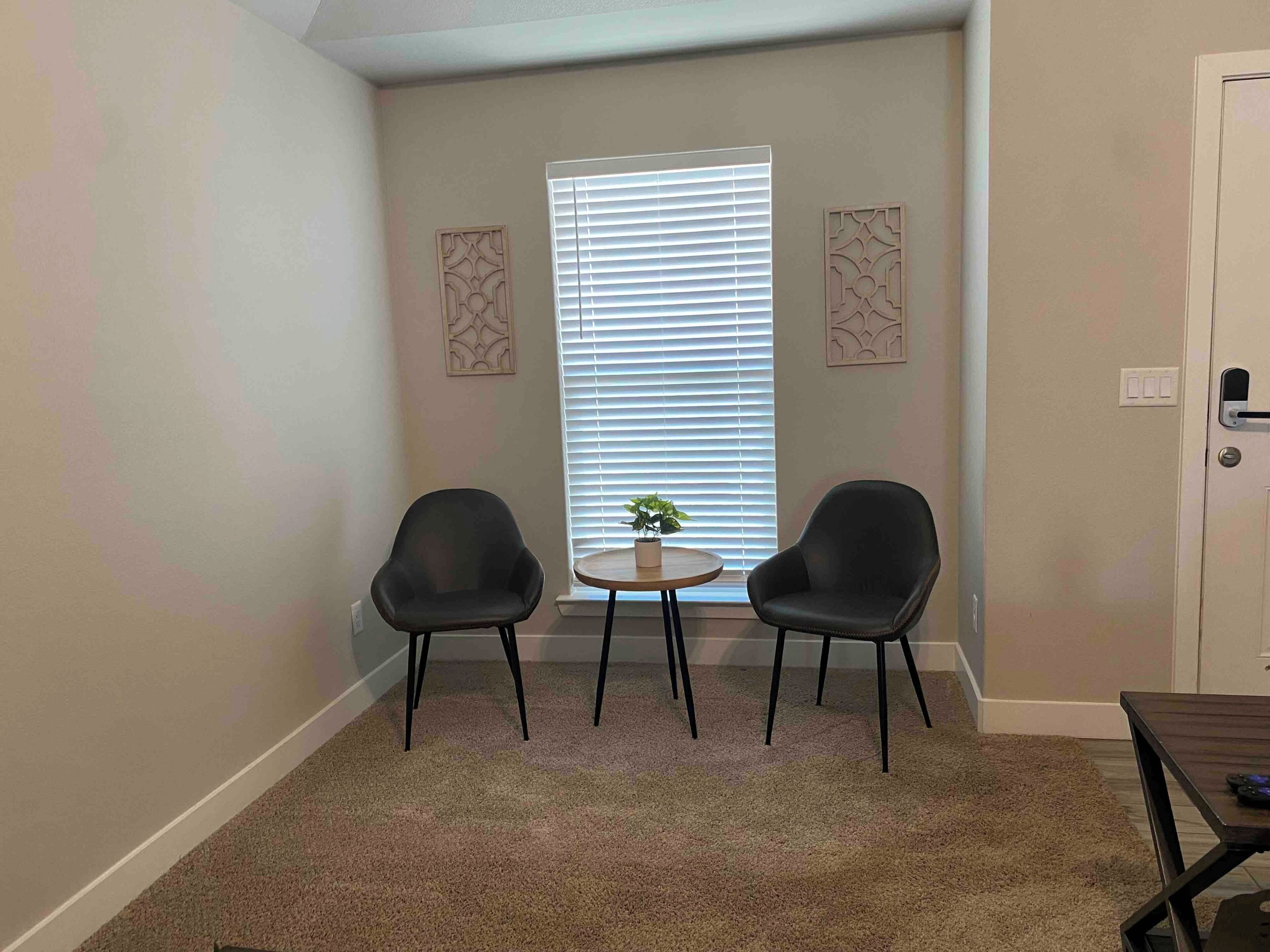 A room with two chairs, a small table, and a window with blinds.