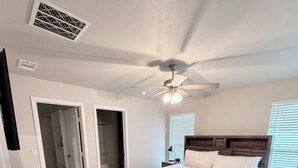 Een slaapkamer met een bed, een plafondventilator, een inloopkast en een deur die naar een andere kamer leidt.