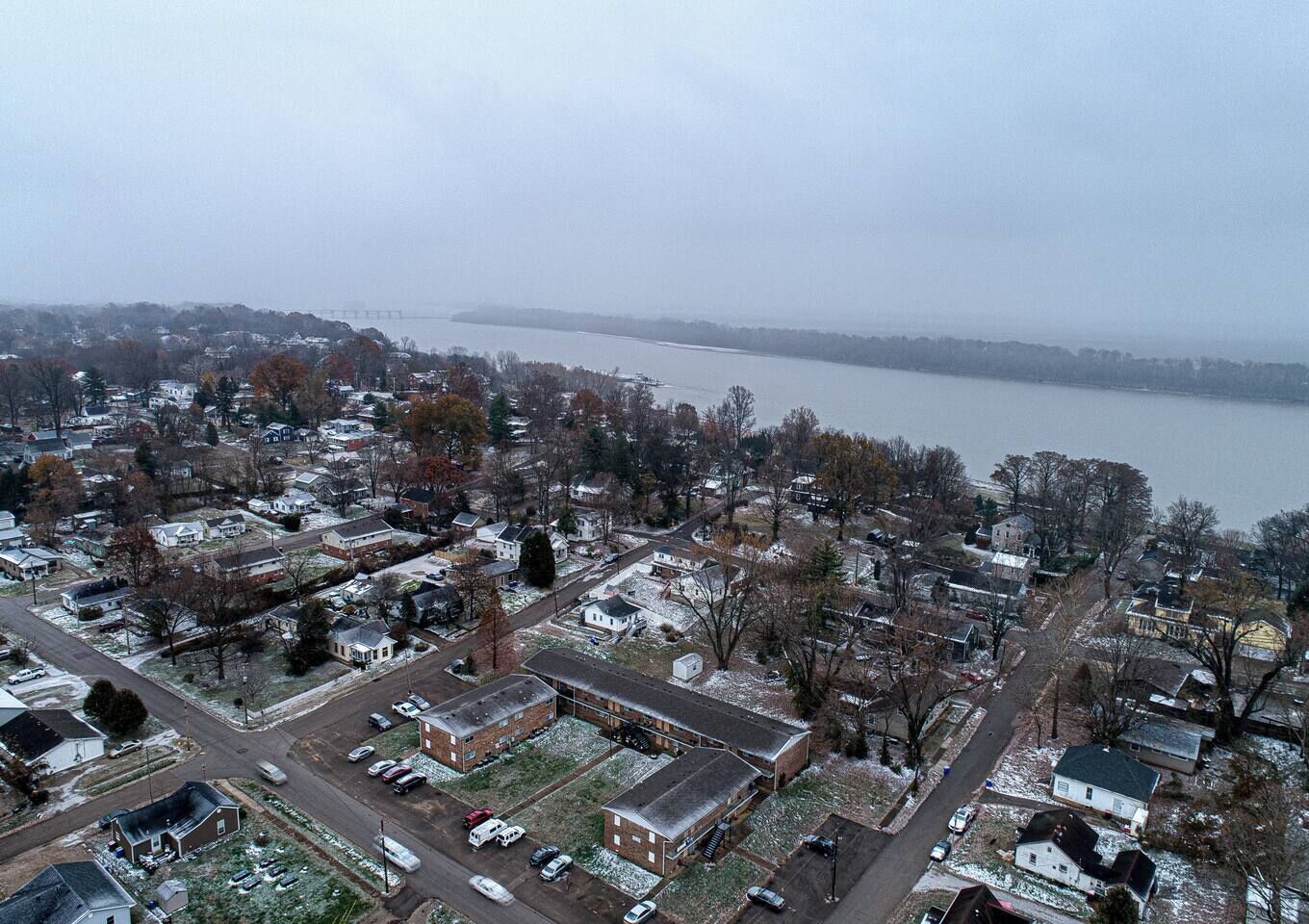 An aerial view of a residential area with houses, a parking lot, and a body of water in the background.