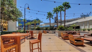 An outdoor patio with wooden furniture, palm trees, and string lights. - Remodeled MGM Signature Suite High FLR  (Las Vegas)