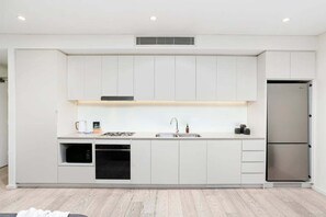 A modern kitchen with white cabinetry, a stainless steel refrigerator, a built-in oven, and a microwave. - ROSE9 - Sunlit Rosebery Stay | Balcony & Easy Airport Access (Sydney)