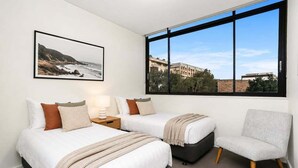 Una camera d'albergo con due letti, una sedia, un'ampia finestra con vista e un quadro appeso al muro.