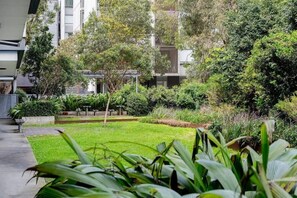 A courtyard with a well-maintained lawn, various plants, and a building in the background. - ROSE9 - Sunlit Rosebery Stay | Balcony & Easy Airport Access (Sydney)
