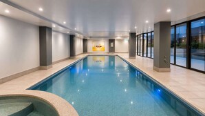 Une piscine avec un jacuzzi, des murs carrelés et de grandes fenêtres.