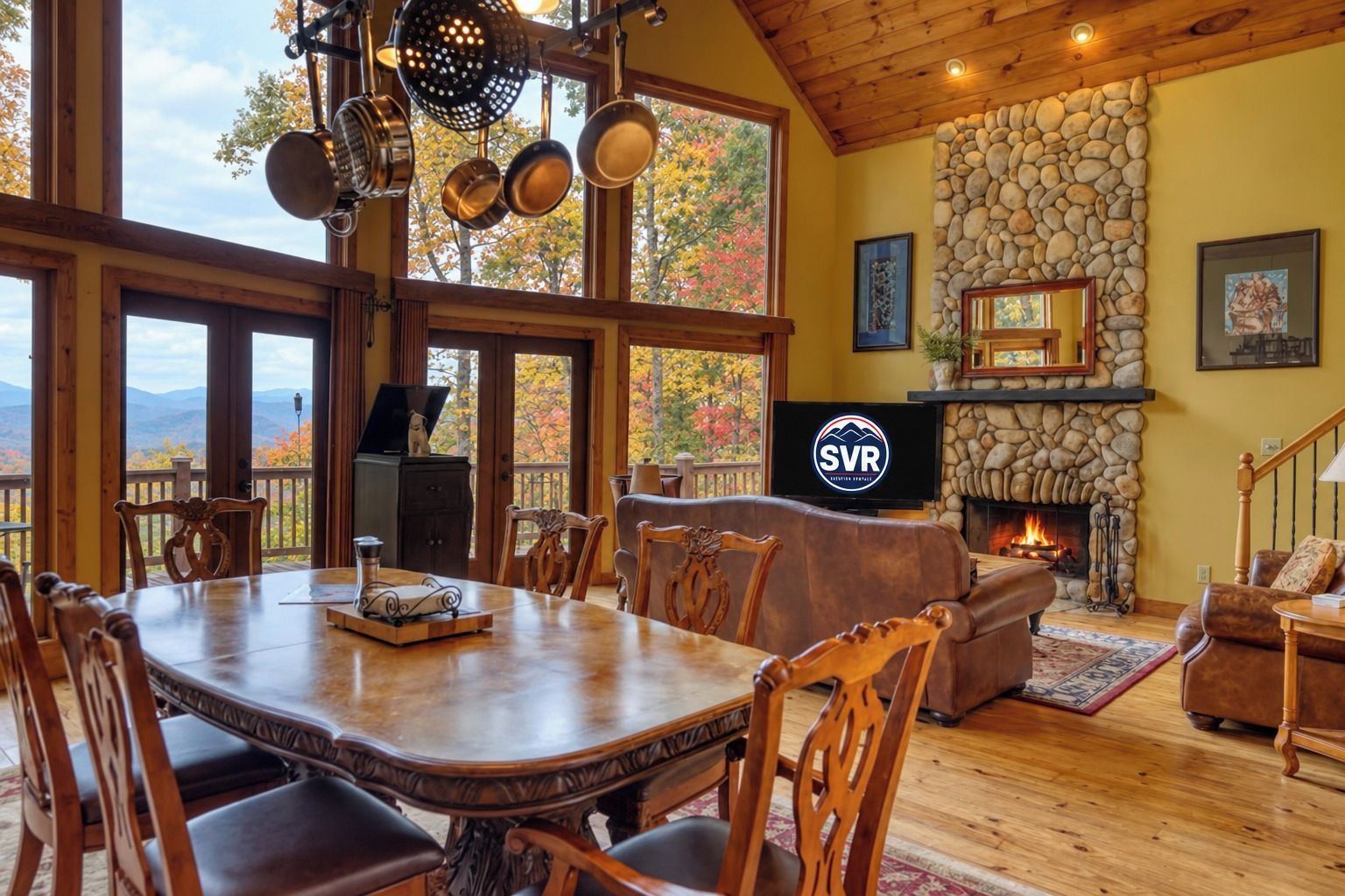 A spacious dining area with a large wooden table and chairs, a stone fireplace, and a television displaying the SVR logo.