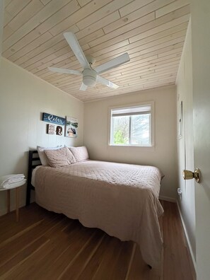 Une chambre à coucher avec un lit, un ventilateur de plafond, une fenêtre et une porte.