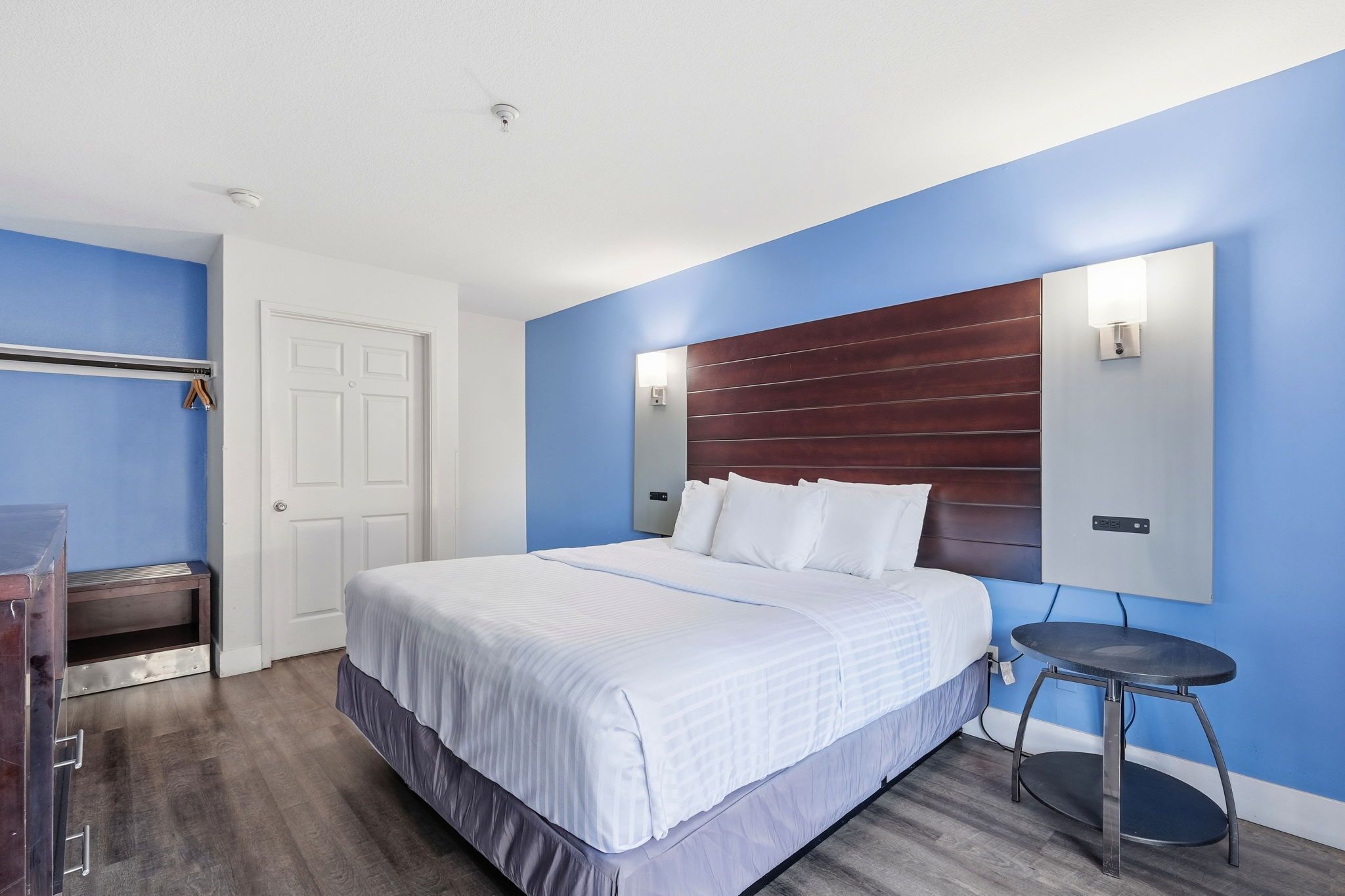 A hotel room with a large bed, a bedside table, a wardrobe, and a wall-mounted light fixture.