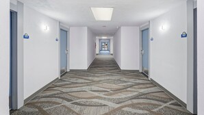 Un pasillo de hotel con pisos alfombrados, paredes blancas y puertas numeradas 117 y 107.