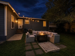 Une maison dotée d’un patio comprenant un foyer extérieur, des sièges de jardin et des guirlandes lumineuses.