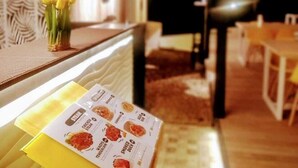 A restaurant interior with a menu on a yellow table, a vase of yellow flowers, and a patterned wall.