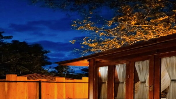 A wooden cabin with a stone pathway leading to a wooden deck over water, surrounded by a wooden fence.