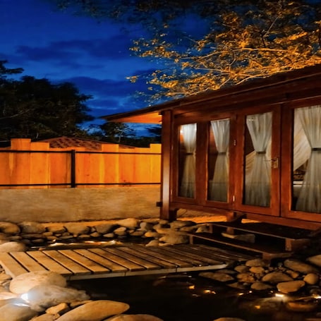 A wooden structure with a stone pathway leading to a pond, surrounded by a wooden fence and trees.. Tentrem Bungalow
