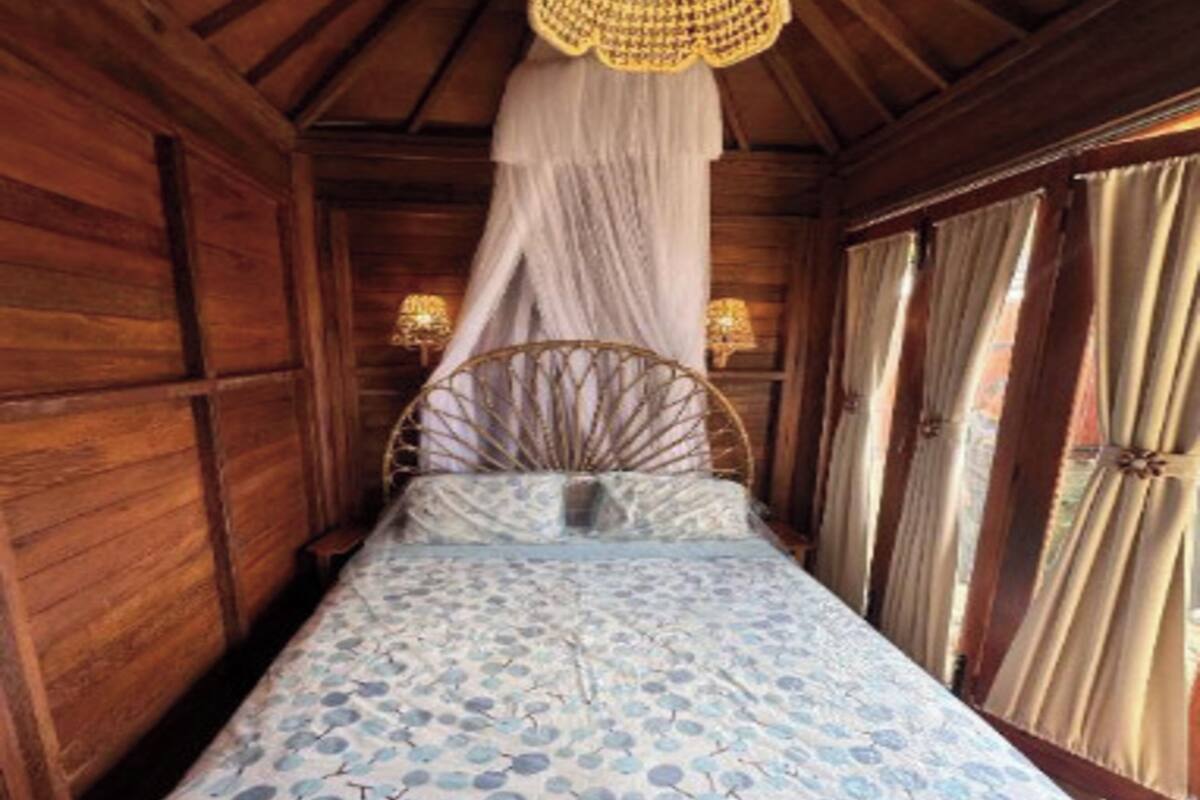 Una habitación de madera con cama, dosel y cortinas.