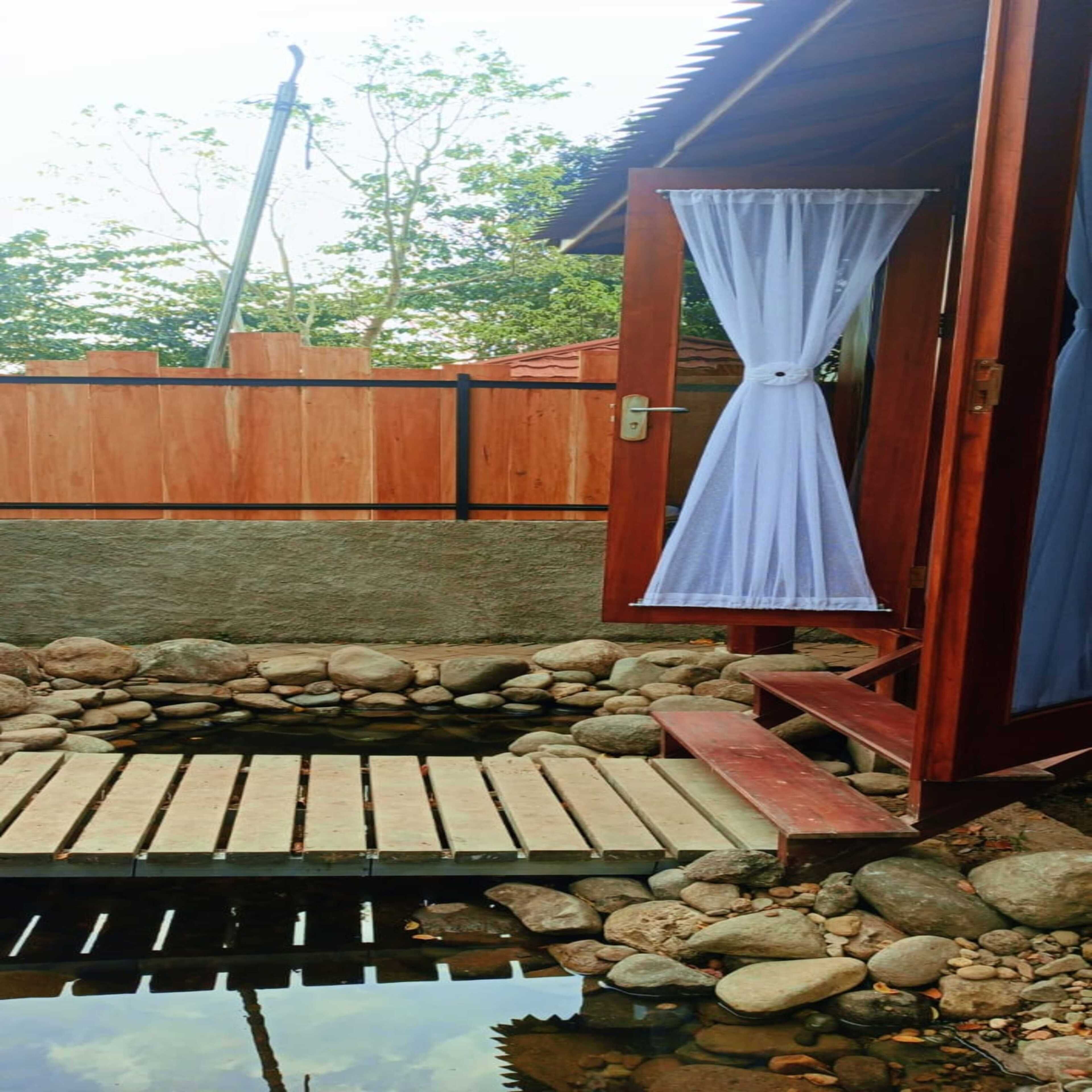 A wooden deck leading to a small pond with a wooden bench, surrounded by rocks and a wooden fence.