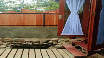 A wooden deck leading to a small pond with a wooden bench, surrounded by rocks and a wooden fence.