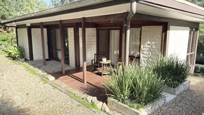 Un espacio al aire libre techado con piso de madera, una mesa con una silla y plantas en macetas.