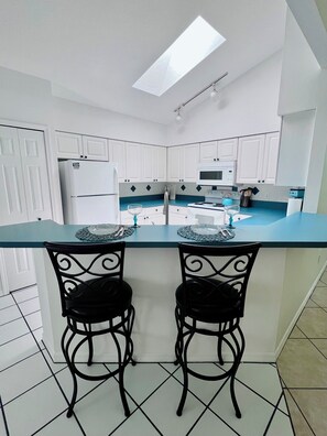 A modern kitchen with white cabinets, a blue countertop, and two black metal chairs. - Spacious Florida Pool Retreat - 15 min from beach (Vero Beach)
