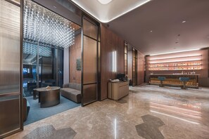Un vestíbulo moderno con zona de estar, mostrador de recepción y un bar con estantes llenos de botellas.