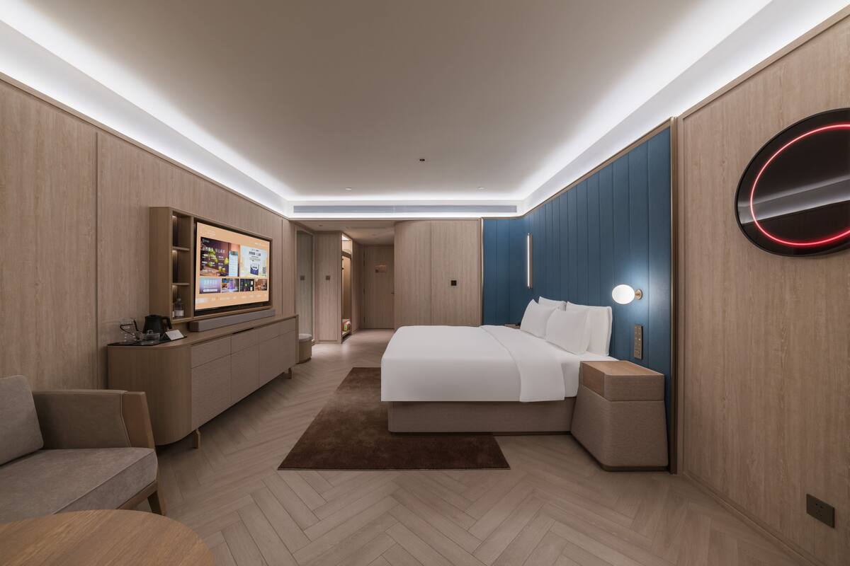 A modern hotel room with a large bed, a TV, a desk, and a seating area.