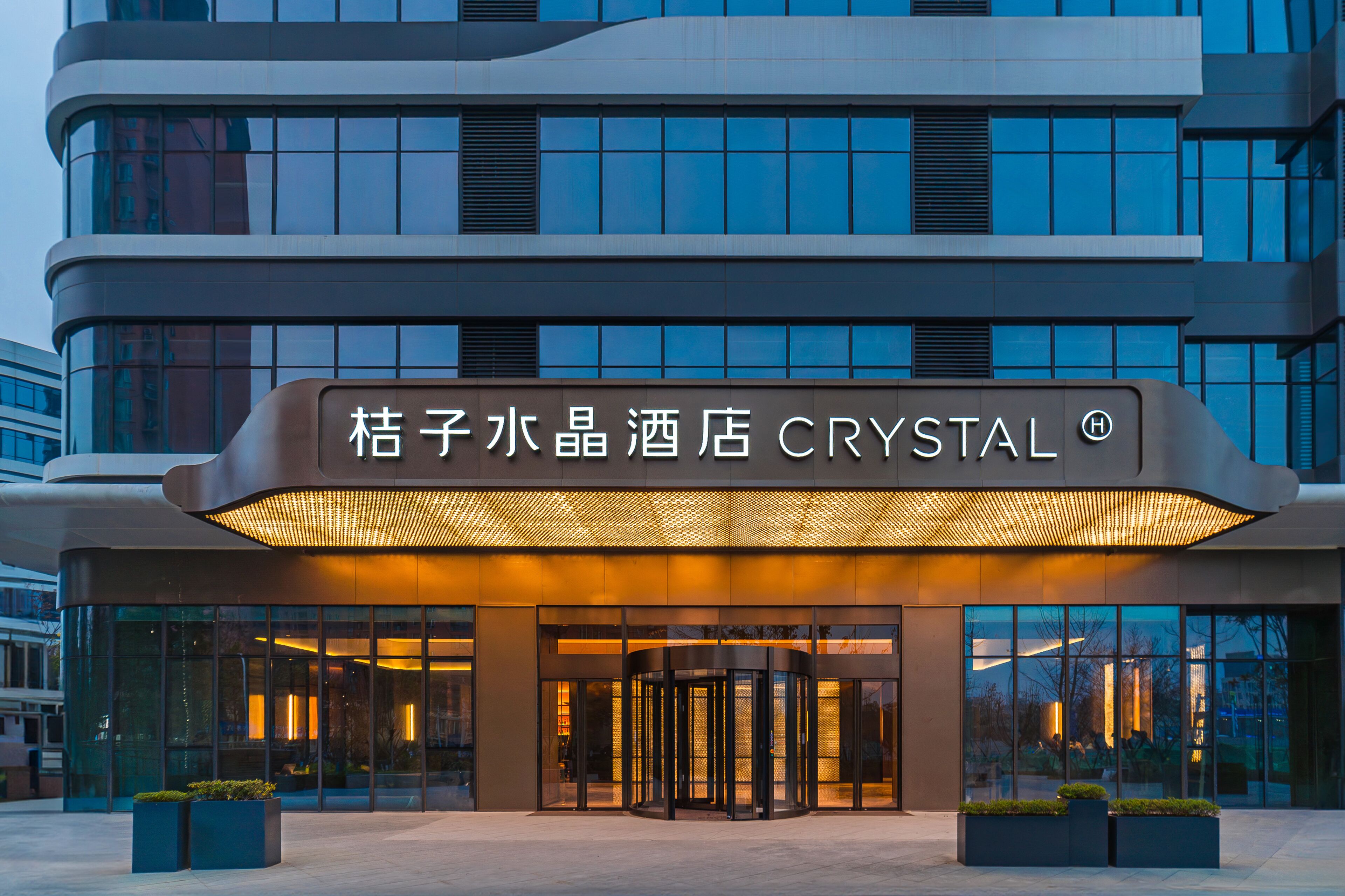Entrada de hotel com porta giratória, grandes janelas de vidro e um letreiro com caracteres chineses.