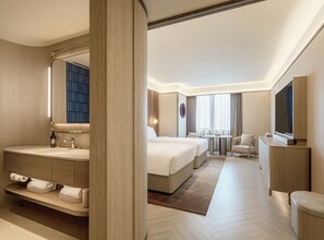 Una habitación de hotel moderna con una cama grande, un área de estar separada, un televisor y un baño con tocador.