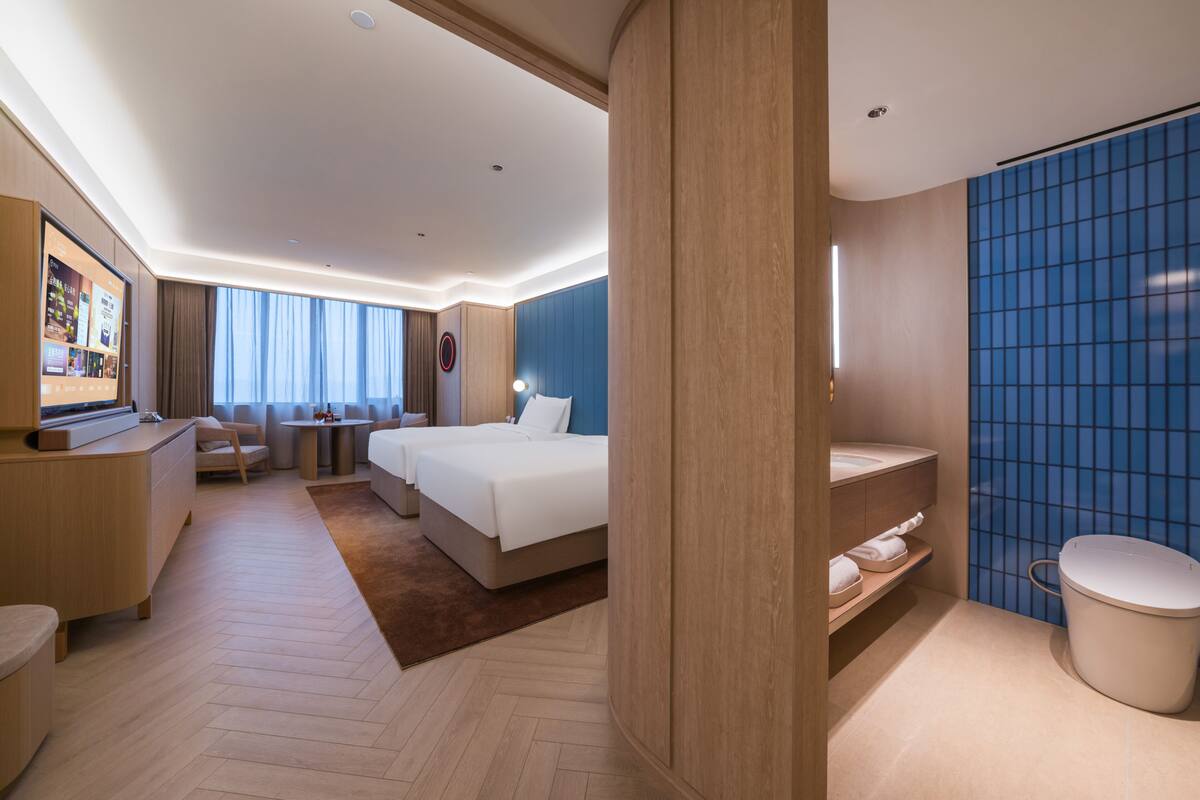 A hotel room with a bed, bedside tables, a desk, a TV, a bathroom with a toilet and sink.