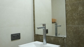 A bathroom with a white sink, a mirror, and a marble countertop. - Arista Stays (Greater Noida)