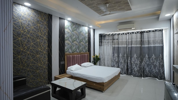 A modern bedroom with a bed, bedside tables, a small table, and a decorative wall. - Arista Stays (Greater Noida)