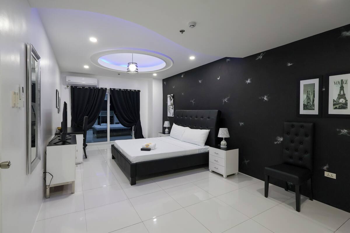 A modern bedroom with a large bed, bedside tables, a chair, and a ceiling light fixture.