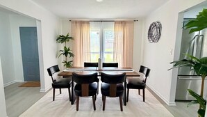 Un coin repas avec une table et des chaises, une fenêtre avec des rideaux, une plante et un réfrigérateur.