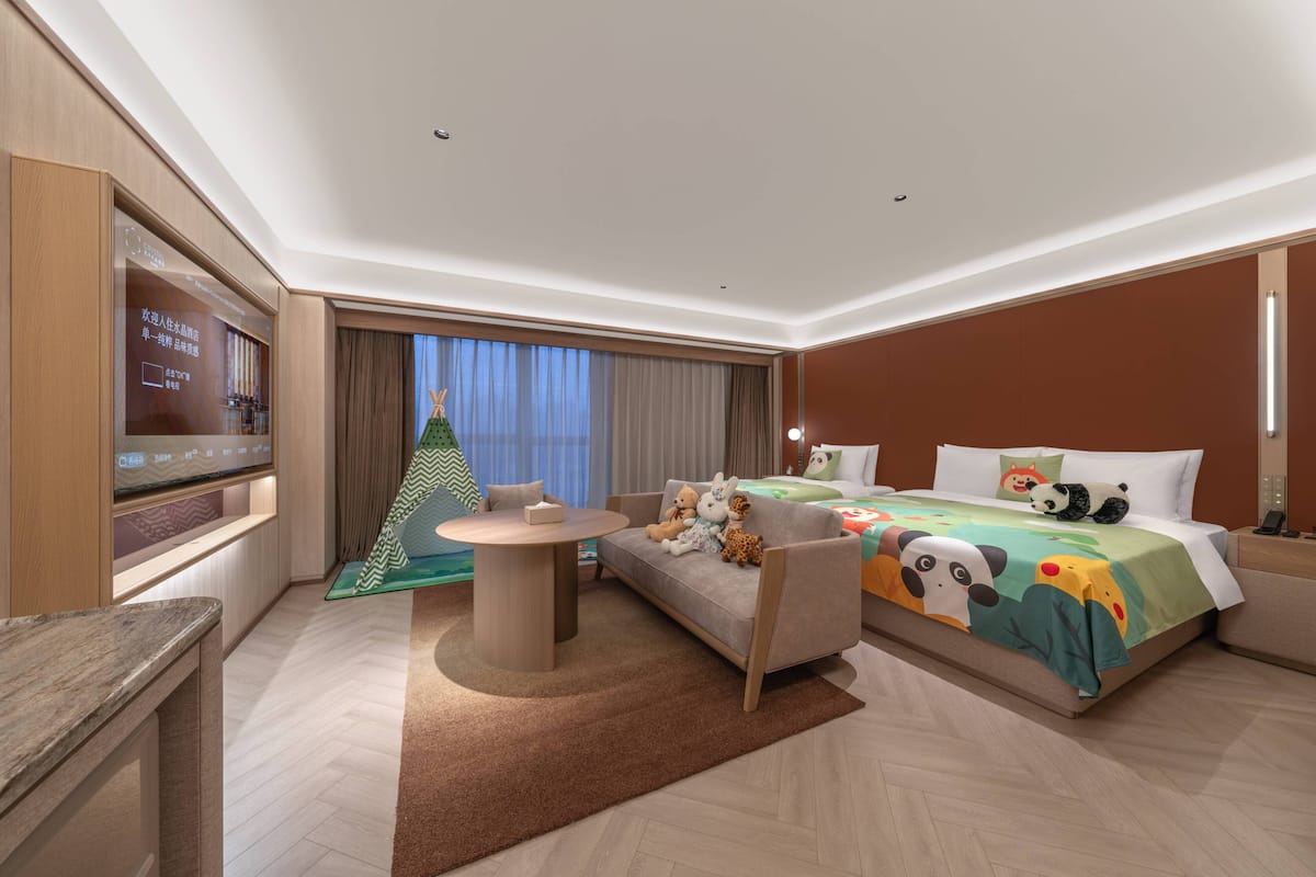 A hotel room with a bed, a sofa, a TV, a small table, and a window with curtains.
