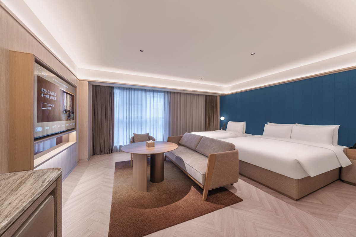 A modern hotel room with a bed, sofa, TV, and a small table.