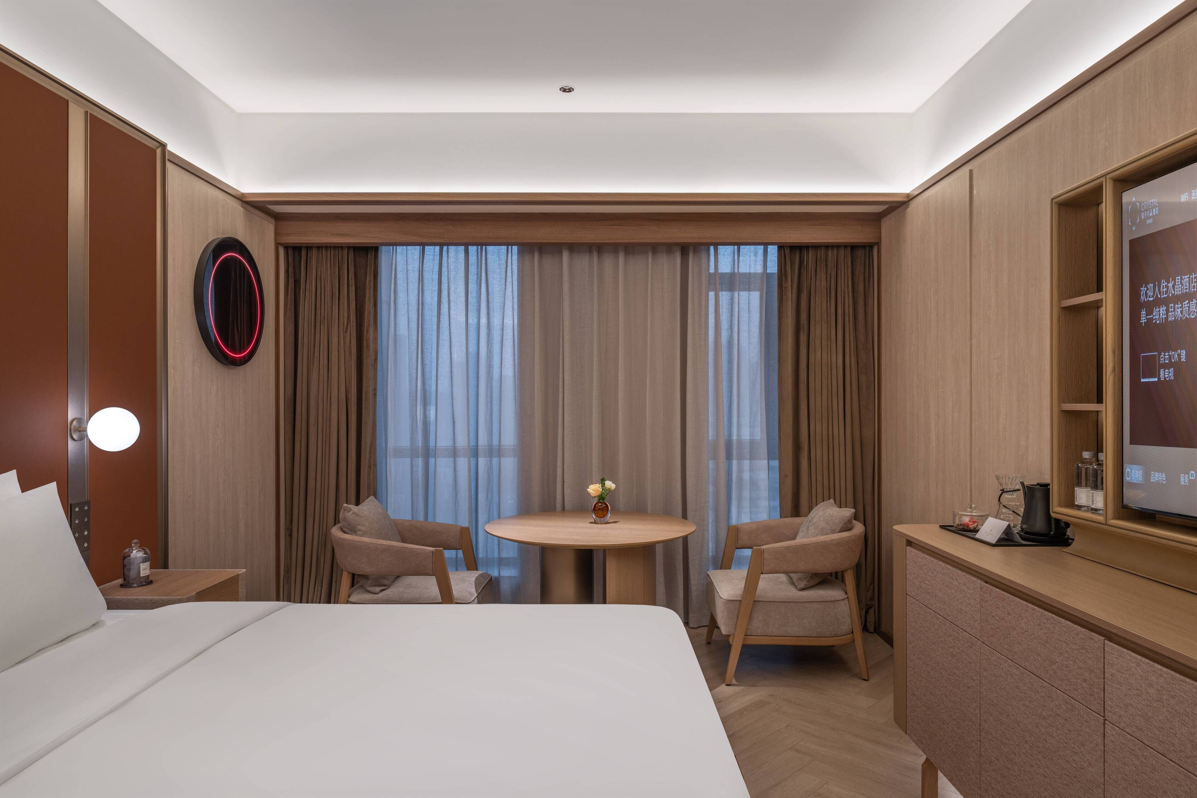 A hotel room with a bed, a round table with chairs, a TV, and curtains.