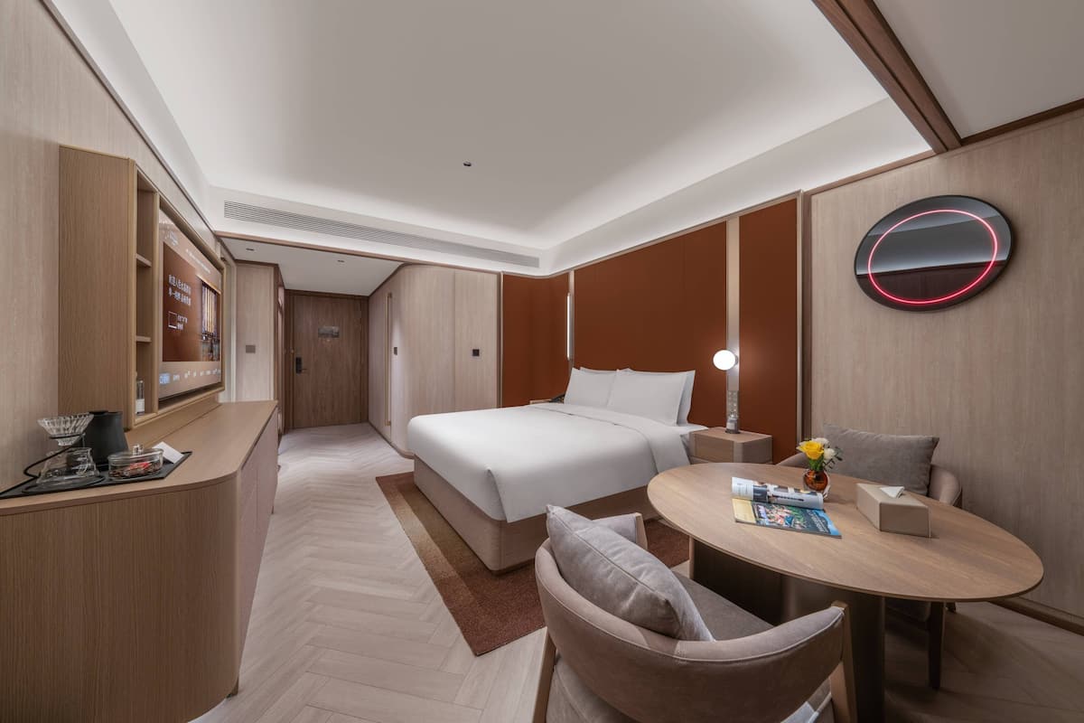 A hotel room with a bed, bedside table, chair, desk, and a round table with a lamp.