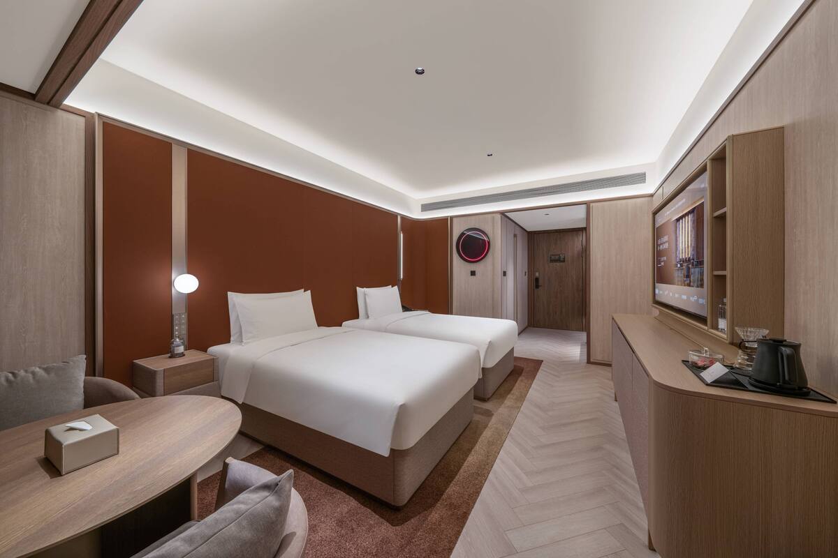 A hotel room with a large bed, bedside tables, a desk, a chair, a lamp, and a TV.