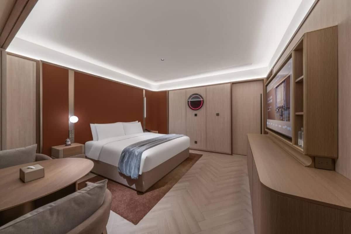 A modern hotel room with a bed, bedside table, lamp, and a TV on a stand.