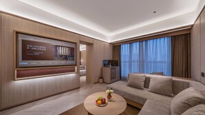A modern hotel room with a large flat-screen TV, a sofa, a coffee table with fruit, and a kitchen area. - Orange Crystal Hotel Chengdu South Railway Station (Chengdu)