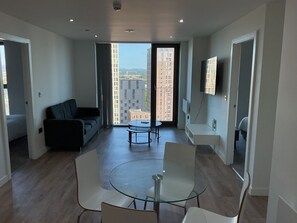 Eine moderne Wohnung mit Glastisch, einer Couch, einem an der Wand befestigten Fernseher und einem Balkon mit Blick auf die Stadt.