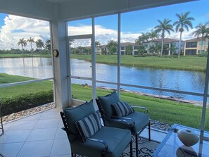 Ein Zimmer mit Seeblick, zwei Sessel mit Kissen, ein Tisch mit einer Vase und eine Uhr an der Wand.