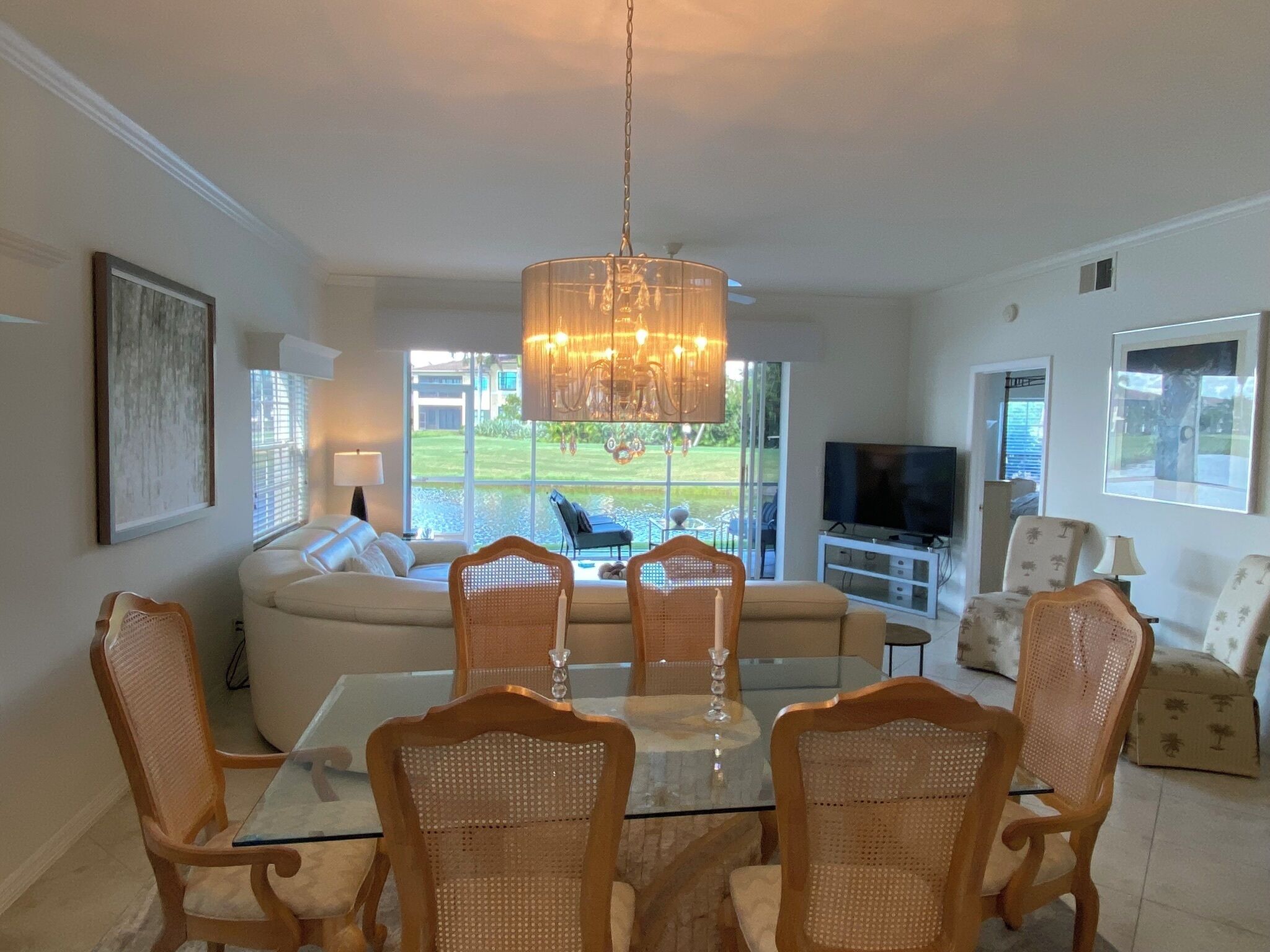 A dining area with a glass table, wicker chairs, a sofa, and a TV in the background.