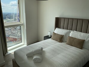 Ein Hotelzimmer mit großem Fenster, einem Bett mit gemusterten Bettwäsche und einem Nachttisch mit Lampe.