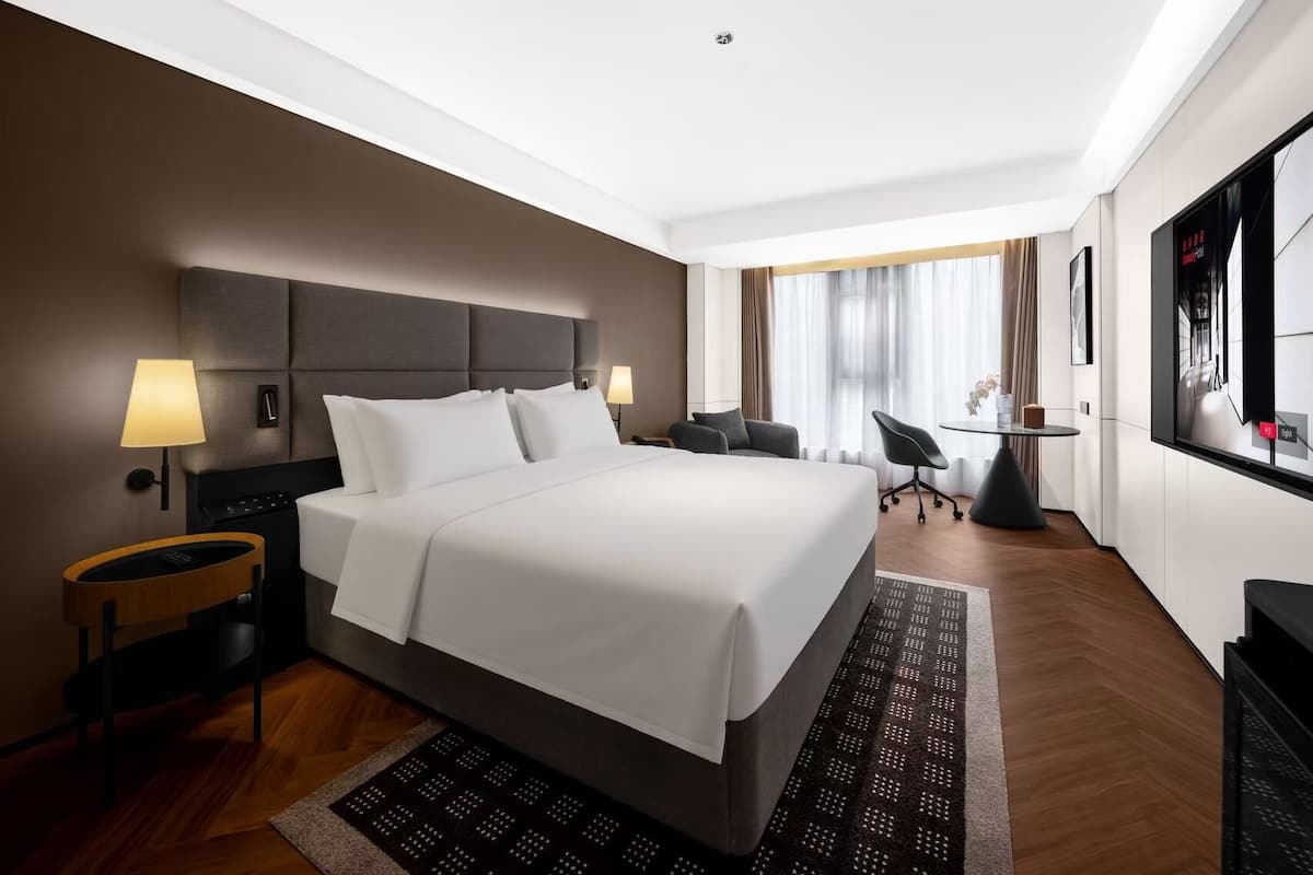 Una habitación de hotel moderna con una cama grande, lámparas de noche, un escritorio y un televisor.