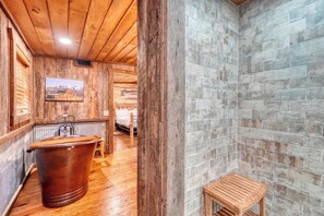 A rustic bathroom with a wooden bathtub, a wooden stool, and a stone wall. - Private 2BR fishing cabin on Cooper Creek w/hot tub. Dog-friendly! (Suches)