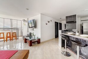 A modern kitchen with a flat-screen TV, a dining area with stools, and a large window. - Rodadero Sol & Mar (Gaira)