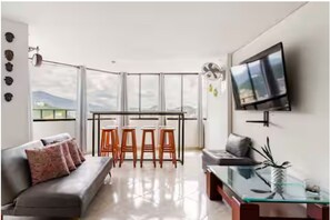 A modern living room with a sofa, a glass coffee table, a TV mounted on the wall, and a balcony with a table and chairs. - Rodadero Sol & Mar (Gaira)