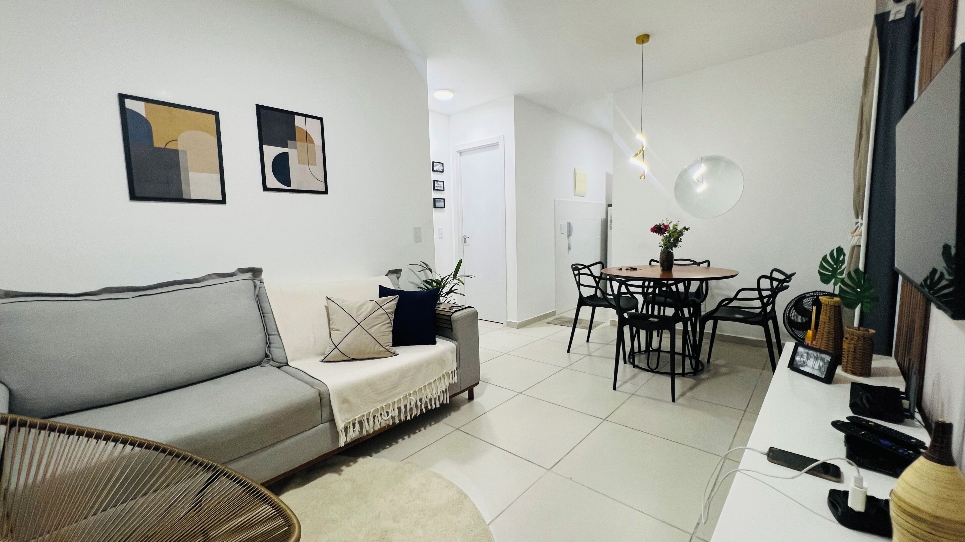 Un salon moderne avec un canapé gris, une table à manger avec des chaises et un meuble pour la télévision, sur lequel est posée une télévision à écran plat.